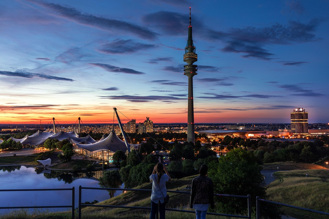 Skyline van München met Olympiatoren bij zonsondergang Zonsondergang uitzicht op de skyline van München met Olympiatoren en verlichte gebouwen die op het water weerspiegelen