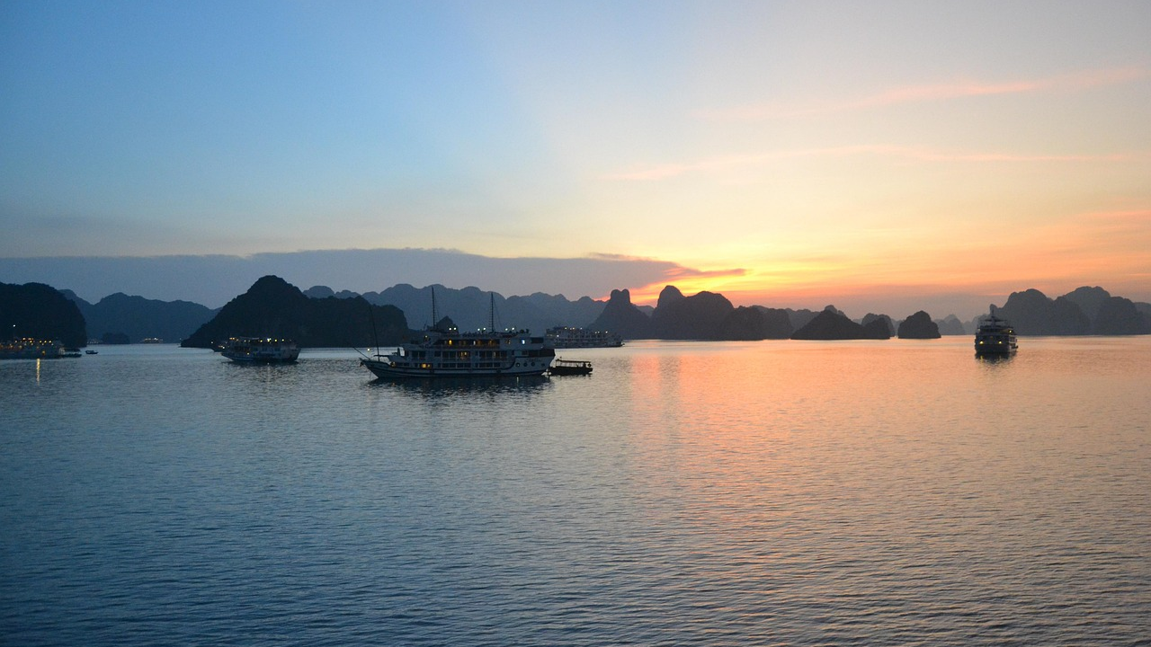 Zonsondergang over kalme zee met traditionele boten en kalkstenen eilanden in Ha Long Bay, Vietnam, die serene natuurlijke schoonheid tonen.