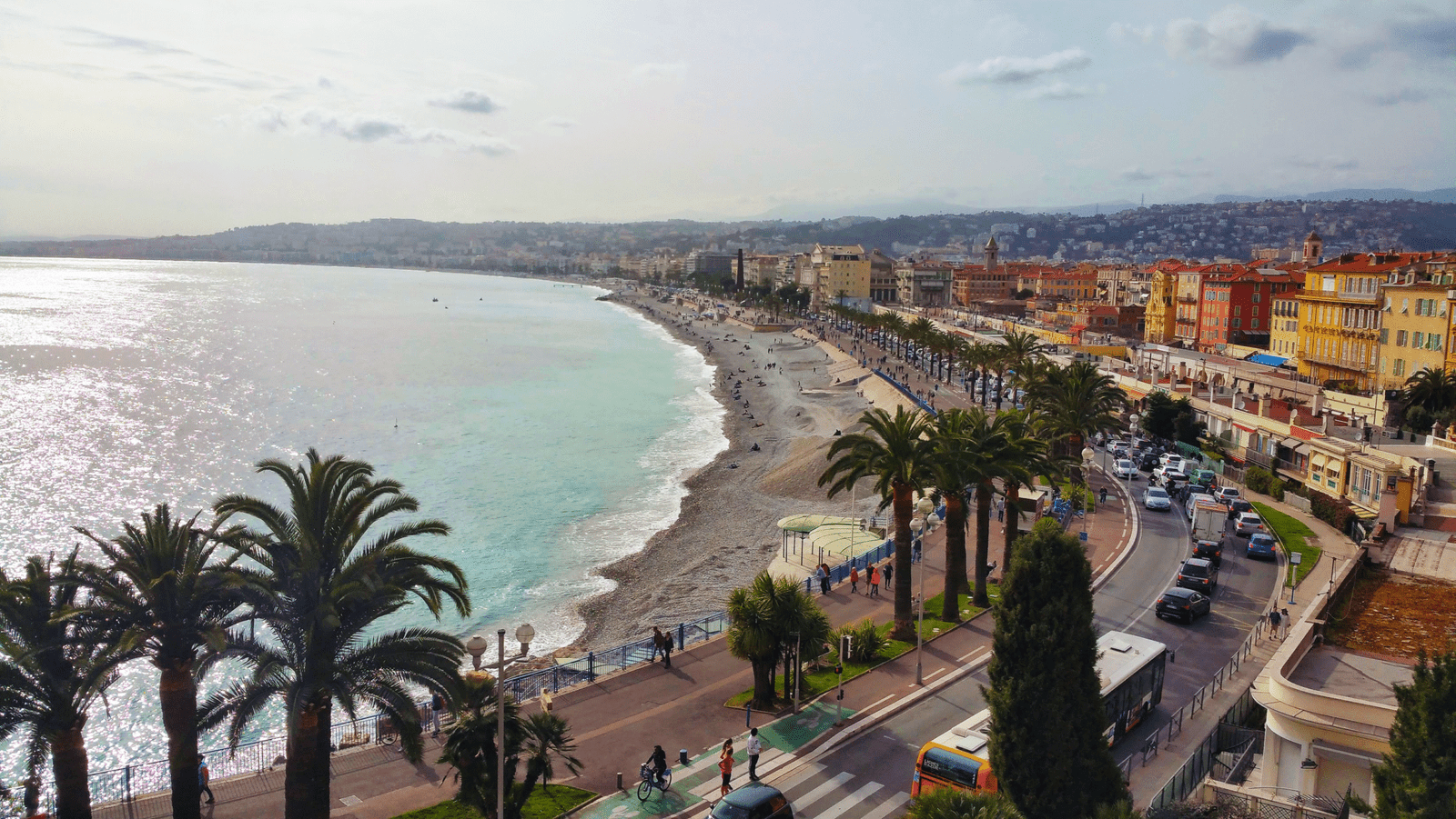 Schilderachtig uitzicht op Nice Promenade des Anglais met palmbomen, kiezelstrand, turquoise zee en levendige stadsgezicht in Frankrijk