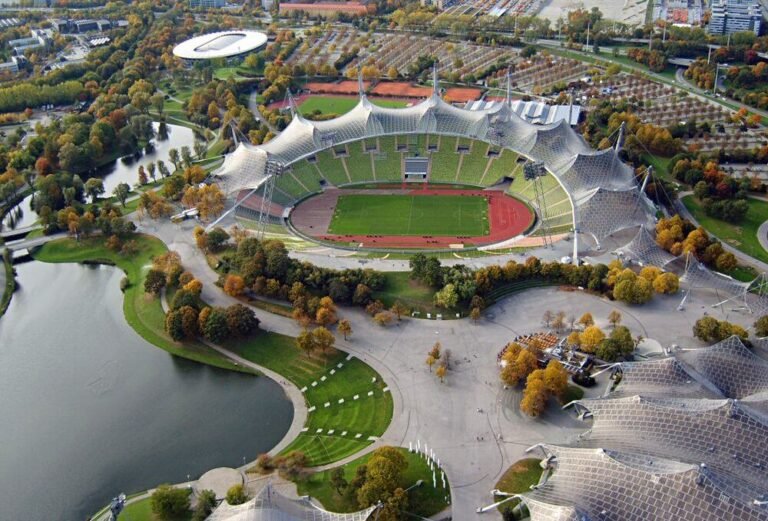 Luchtfoto van het Olympiastadion van München met zijn karakteristieke tentdak, te midden van de meren en bomen van het Olympiapark