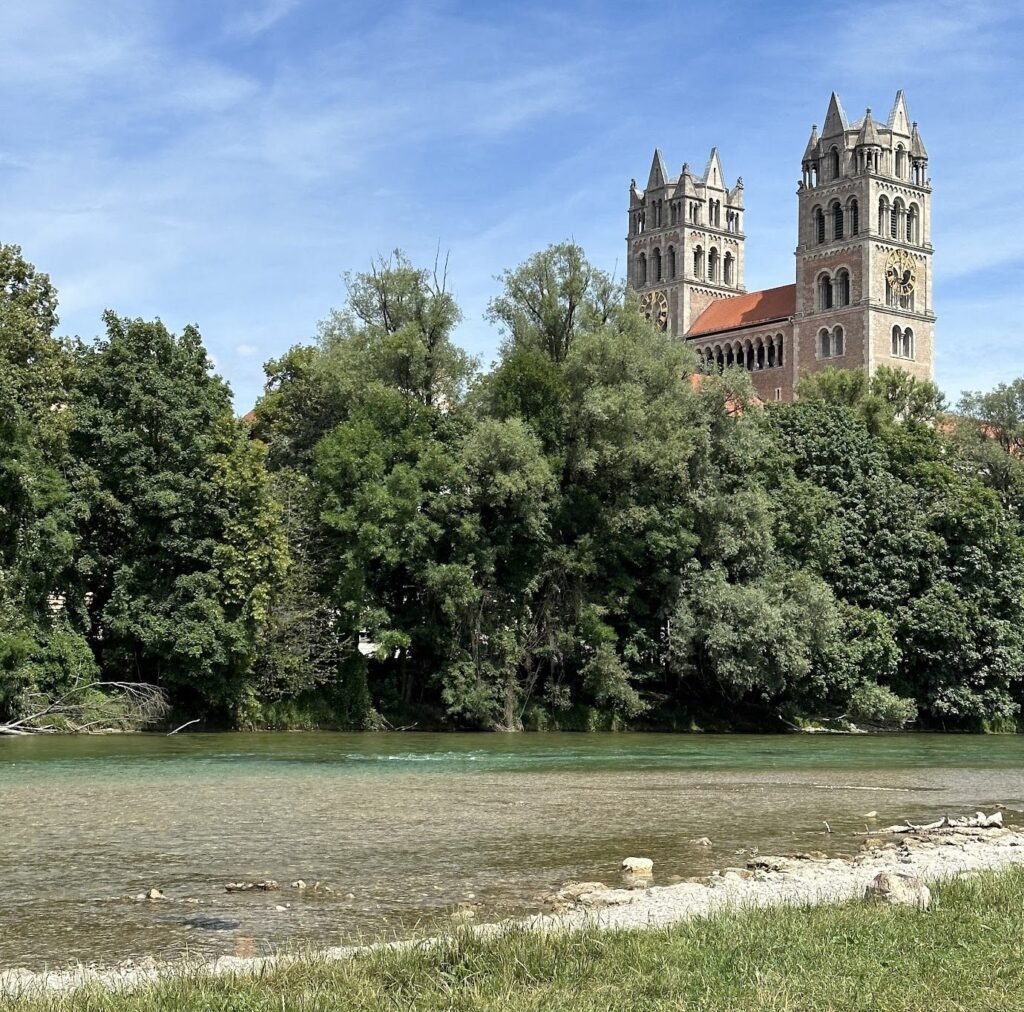 De twee torens van de St.-Maximiliankerk boven de groene oevers van de Isar in München