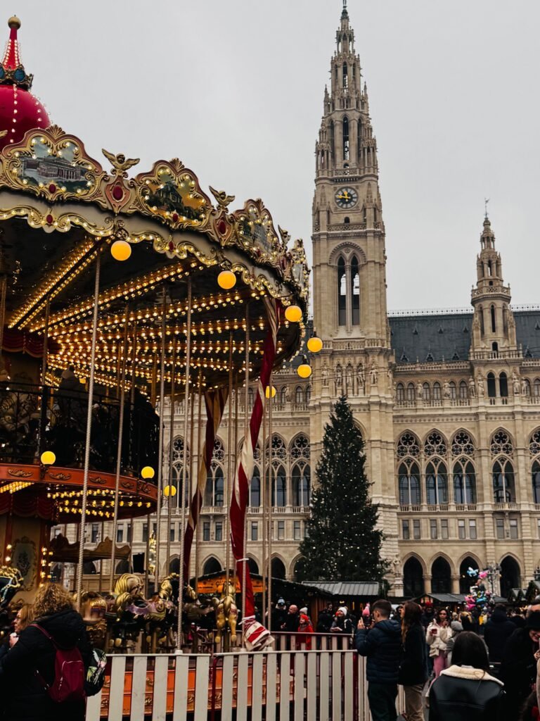 De Christkindlmarkt van Wenen bij het Rathaus, met een verlichte carrousel en kerstboom voor het gotische stadhuis